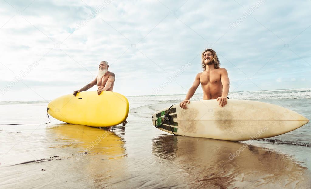 Happy fit friends having fun surfing on tropical ocean - Surfers father and son doing stretching surf exercises - Sporty people lifestyle and extreme sport concept