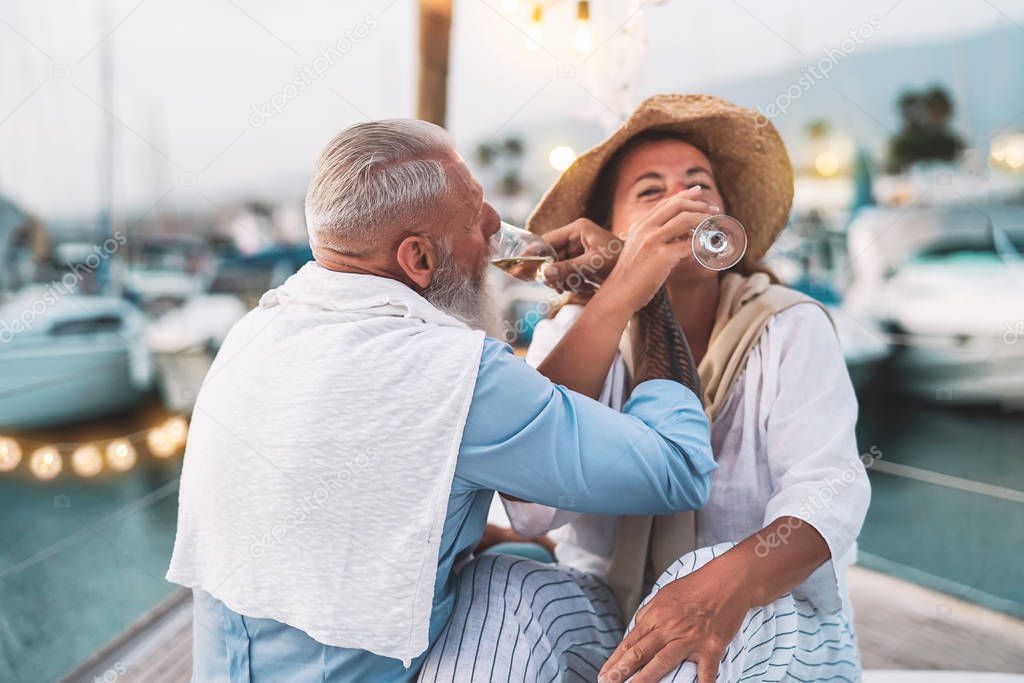 Senior couple date drinking champagne on sailboat vacation - Happy elderly people having fun celebrating wedding anniversary on boat trip - Relationship love and romantic travel dating concept