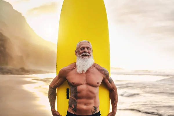 Glücklich fitter Senior mit Spaß am Surfen bei Sonnenuntergang - Sportlicher bärtiger Mann trainiert mit Surfbrett am Strand - Gesunder Lebensstil älterer Menschen und Extremsportkonzept — Stockfoto