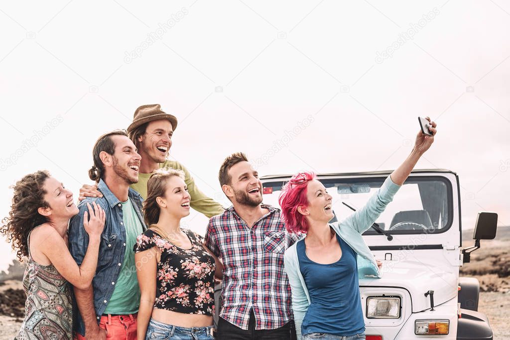 Happy friends taking selfie with mobile smartphone next offroad convertible car - Millennial young people having fun making road trip - Vacation, tech and youth holidays lifestyle concept