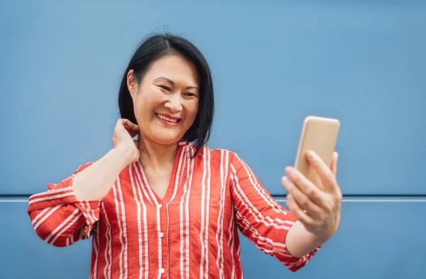 Mujer asiática feliz usando teléfono inteligente móvil al aire libre - Senior divertirse con la nueva tecnología de moda para aplicaciones de redes sociales - Tecnología de estilo de vida de ancianos y el concepto de personas mayores —  Fotos de Stock