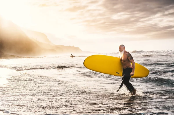 Happy fit senior surfing on sunset time - Sporty mature man having fun training with surfboard in ocean - Elderly healthy people lifestyle and extreme sport concept — Stock Photo, Image