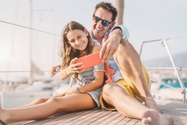 Baba ve kızı yelkenli gezisi sırasında selfie akıllı telefon kamerası kullanıyor - Mutlu aile tatilde sosyal medya için yeni mobil uygulamalarla eğleniyor - insanların yaşam tarzı ve teknoloji konseptini gezmek