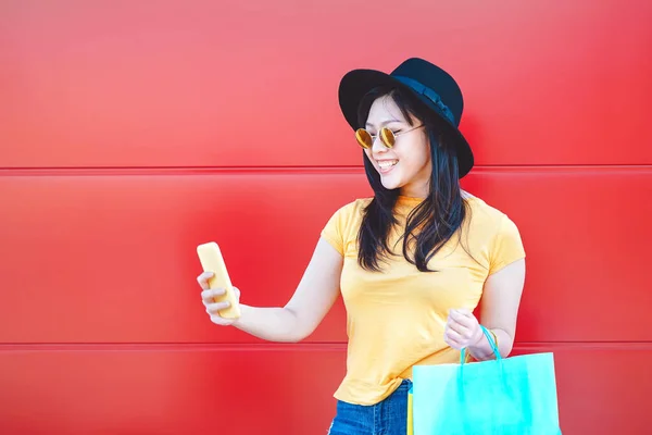 Aziatisch mode meisje doet winkelen in winkelcentrum met behulp van mobiele smartphone - Gelukkig Chinese vrouw heeft plezier met het kopen van nieuwe kleren in vakantie - Consumentisme, mensen en jeugd lifestyle concept — Stockfoto