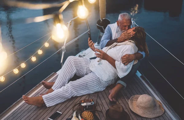 Pareja mayor besándose durante las vacaciones en velero - Personas maduras felices teniendo momentos tiernos celebrando aniversario de boda en viaje en barco - Relación de amor y concepto de estilo de vida de viaje —  Fotos de Stock