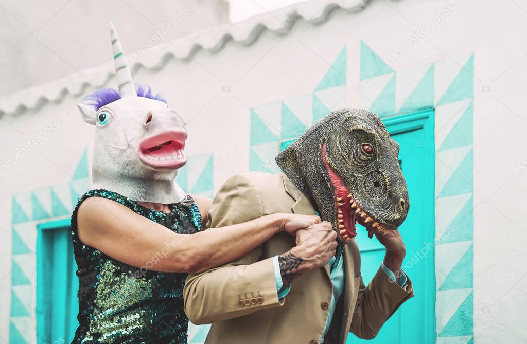 Crazy senior couple wearing unicorn and t-rex mask while dancing outdoor - Mature trendy people having fun celebrating carnival time - Absurd concept of masquerade funny holidays