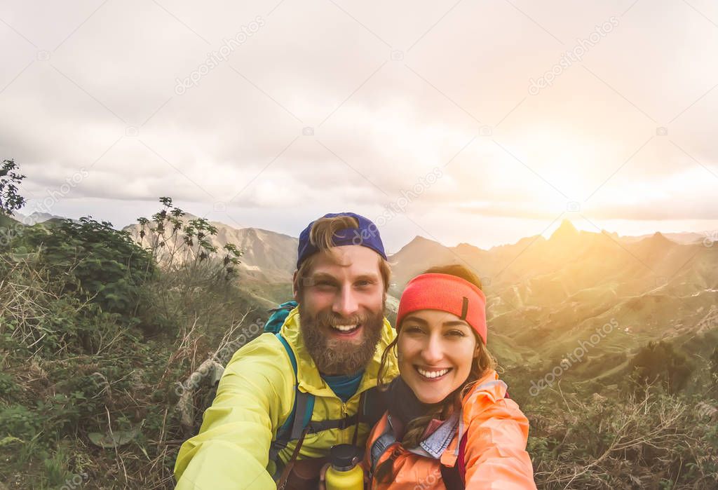 Happy couple taking selfie while doing trekking excursion on mountains - Young hikers having fun on exploration nature tour - Relationship and travel vacation lifestyle concept
