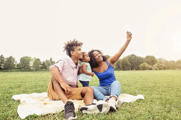 快乐的非洲家庭在户外的公共公园里用手机做自拍照片--父母在周末阳光明媚的日子里和女儿一起玩--爱情和幸福的概念 — 图库照片