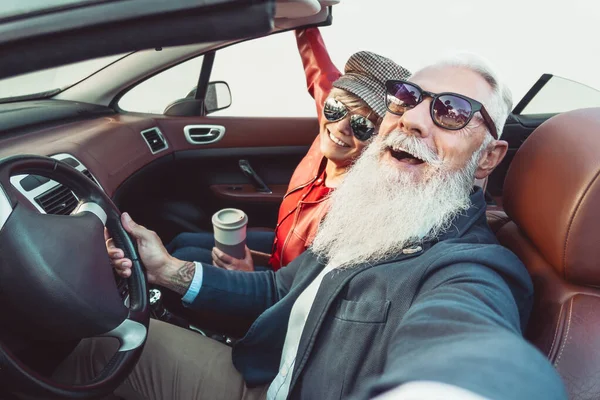 Happy senior couple taking selfie on new convertible car - Mature people having fun together during road trip vacation - Elderly lifestyle and travel transportation concept — Stock Photo, Image