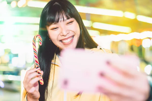 Asian girl taking selfie with mobile phone in amusement park - Happy woman having fun with new trends smartphone apps - Youth millennial people generation and social media addiction concept — Stock Photo, Image