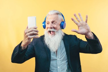 Kulaklıkla müzik dinlerken selfie çeken mutlu kıdemli adam - Hippi sakallı erkek cep telefonu çalma listesi uygulamaları kullanarak eğleniyor - teknoloji ve yaşlılar yaşam tarzı kavramı