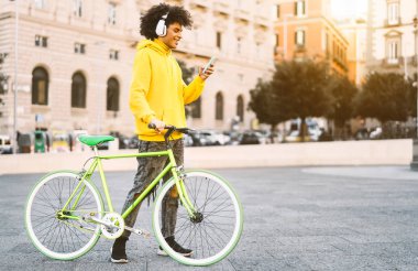 Mutlu Afro adam dışarıda cep telefonu kullanıyor - genç adam şehirde bisiklet sürerken kulaklıkla müzik dinlerken eğleniyor - genç nesil yaşam tarzı ve teknoloji konsepti