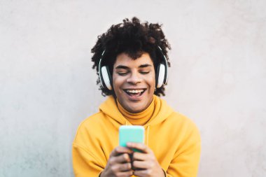 Mutlu Afro adam dışarıda cep telefonu kullanıyor genç adam dışarıda kablosuz kulaklıkla müzik dinlerken eğleniyor genç adam genç nesil yaşam tarzı ve insanlar teknoloji konseptine bağımlı