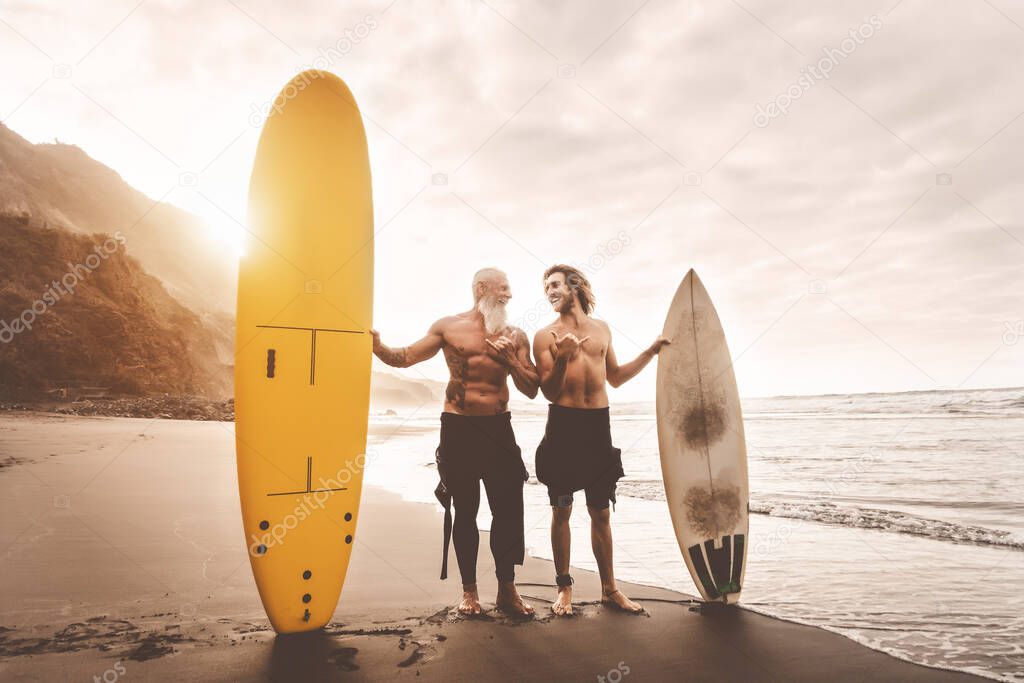 Happy friends surfing together on tropical ocean - Sporty people having fun during vacation surf day - Elderly and youth extreme sport lifestyle concept