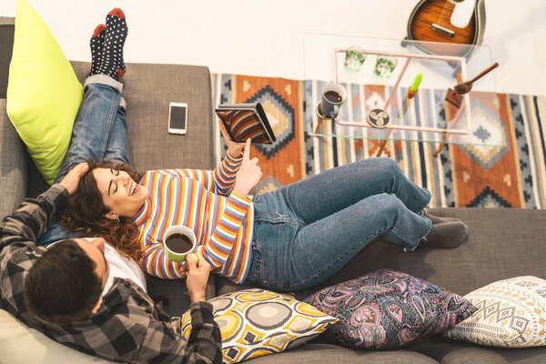 Счастливая пара с помощью планшета во время отдыха на диване дома - Молодые романтические любители весело с новыми технологическими трендами устройства - Технологии и любовь отношения молодежной культуры концепции образа жизни
