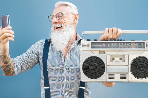 Senior crazy man using phone while listening music with vintage boombox - Hipster guy having fun using mobile smartphone playlist apps - People happiness and elderly technology addicted concept