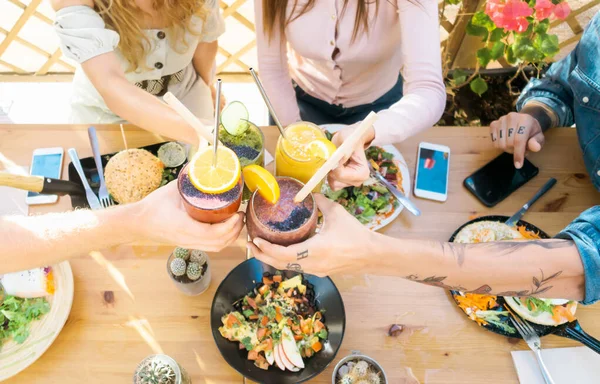 Happy friends cheering with fresh smoothies while lunching together - Young people having fun eating in coffee brunch vintage bar - Healthy food trends and youth lifestyle culture concept