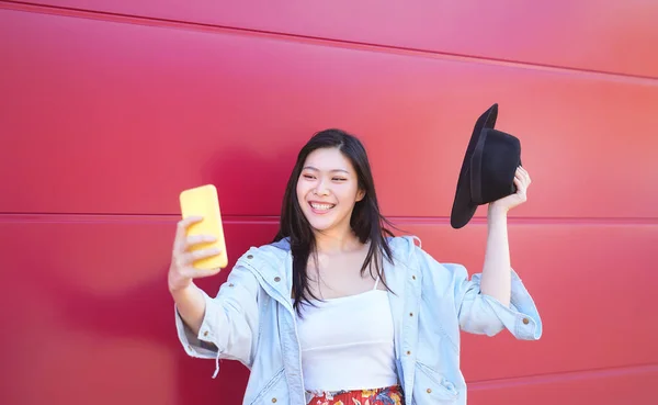 Happy Asian girl taking selfie with mobile smart phone outdoor - Young influencer having fun with new trends social networks apps - Millennial generation lifestyle people technology