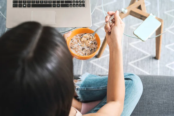 ソファに座ってコンピュータ上で見ている間 牛乳と女性の食べるシリアルカップをトップビュー 健康的な食事とリビングルームのエンターテイメントコンセプト — ストック写真
