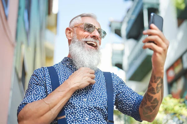 Hipster senior using mobile phone outdoor - Bearded mature man having fun with new trends smartphone apps - Elderly people lifestyle and social media technology concept