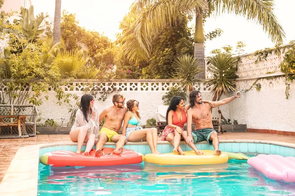 Happy friends making pool party taking selfie with mobile smartphone - Young millennial people having fun in exclusive tropical resort vacation - Summer holidays and youth people lifestyle