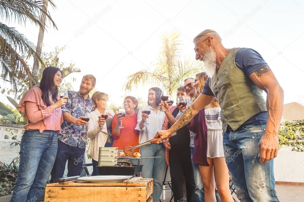 Happy family drinking red wine in barbecue party - Chef senior man grilling meat and having fun with parents - Weekend food bbq and reunion young and older people lifestyle concept