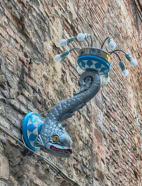 SIENA, ITALY - ИЮНЬ 22: Уличный фонарь с символом Contrada dell 'Onda, район Сиены. Это один из 17 контрадов города, представители которого едут верхом на лошадях в Палио ди Сиена, дважды в год
