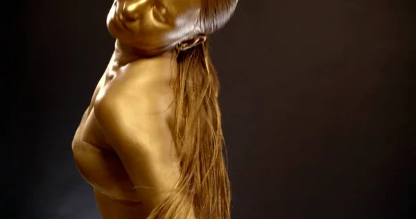 Close-up of an active girl in the Studio on a black background with gold pigment on her skin. Whispers, dancing Oriental belly dance. She has a tail on her head.