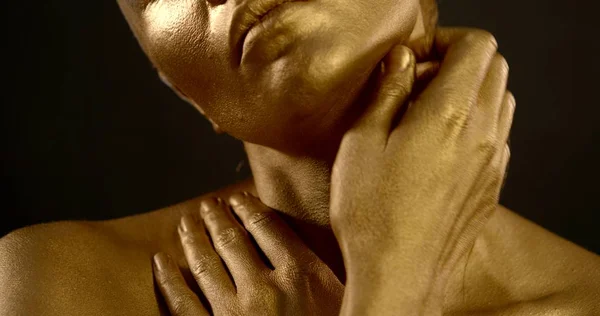 Close-up portrait of a gentle naked girl, she is in the Studio on a black background, she has a Golden pigment on her skin. She poses, makes massage movements with her hands on her shoulders.