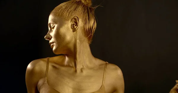 a gentle girl, she is in the Studio on a black background, she has a Golden pigment on her skin. She is wearing a bra, she poses, makes movements with her hands on the body.