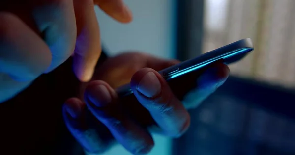 man is using mobile phone in darkness, tapping and swiping on screen, closeup