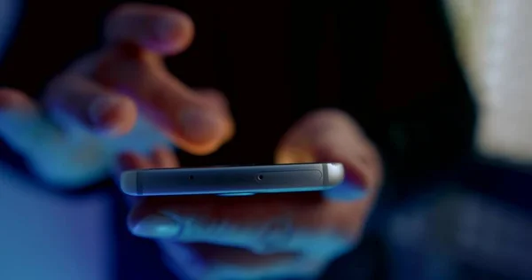 close-up of the end part of the smartphone. the man holds the phone with one hand, and the fingers of the other poke at the screen, which lights up and goes out. lower blue light