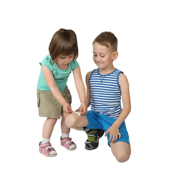 Little girl sticks patch on elder boy knee — Stock fotografie