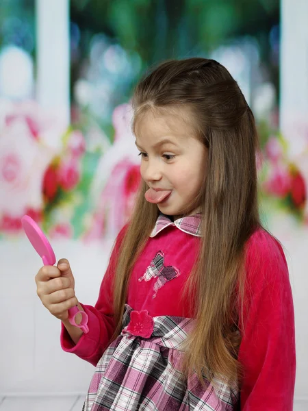 Schattig meisje toont haar tong in spiegel — Stockfoto