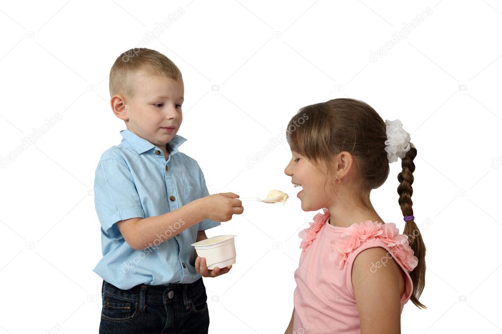 Little boy feeds girl by yogurt with spoon focus on girl and spo