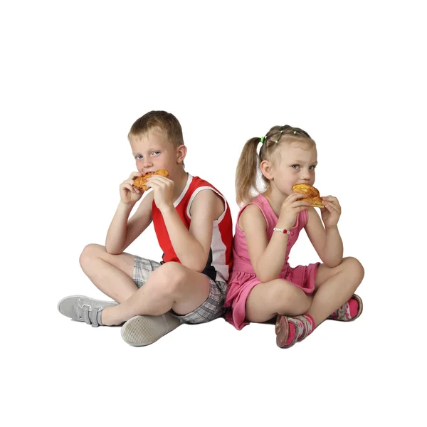 Chico y una chica comen bollos sentados en el suelo —  Fotos de Stock