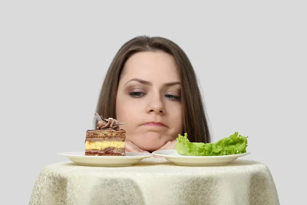 Young woman chooses between cake and lettuce — Stock Photo, Image