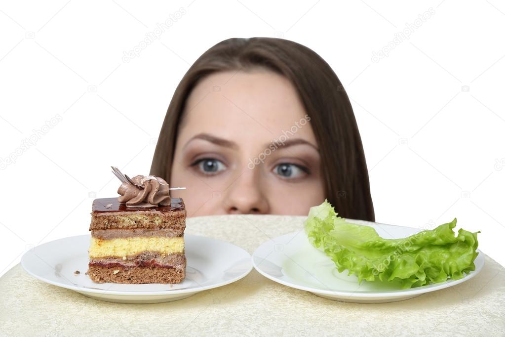 Young woman chooses between cake and lettuce