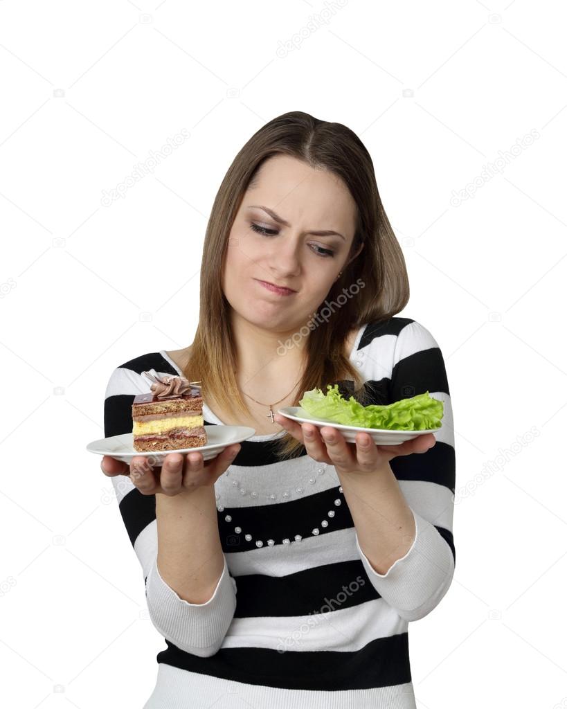 Young woman makes choise between cake and lettuce