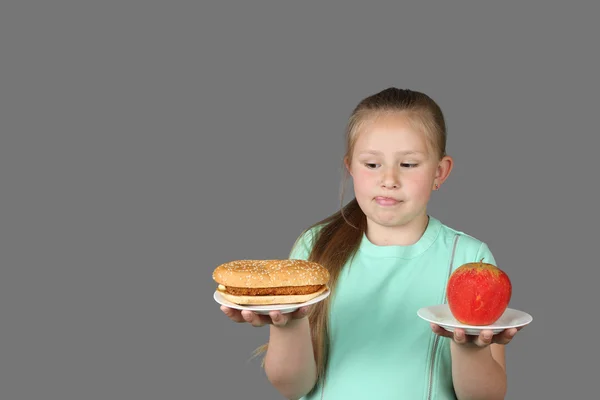 Cute little girl makes choice between hamburger and apple — Stock Photo, Image