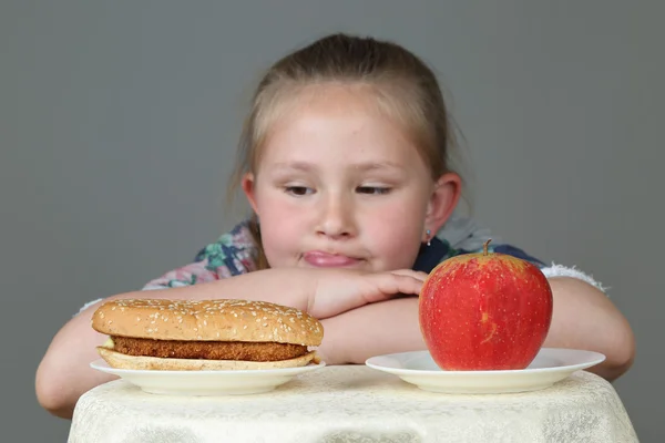 Cute little girl makes choice between hamburger and apple — Stock Photo, Image