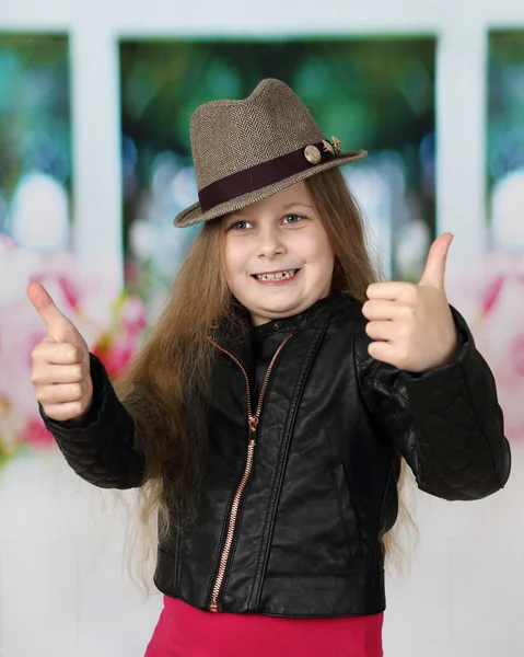 Красивая маленькая девочка с длинными волосами в черной шляпе показывает большие пальцы вверх — стоковое фото