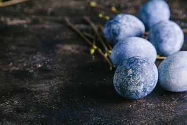 Mutlu Paskalyalar. Çok renkli paskalya yumurtaları mavi tonlarda ve dallarda kahverengi arka planda tomurcuklar ile boyanmış. Kapat, boşluğu kopyala.