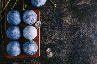 Mutlu Paskalyalar. Çok renkli Paskalya yumurtaları yumurta kutusunda mavi tonlarda ve dalları kahverengi arkaplanda boyanmış. Düz konum, üst görünüm, kopyalama alanı.