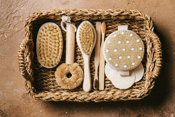 Zero waste concept. Set of brush for washing dishes, brushes for massage, toothbrushes in a wicker basket on a beige background. Eco friendly and reuse concept. Close up.