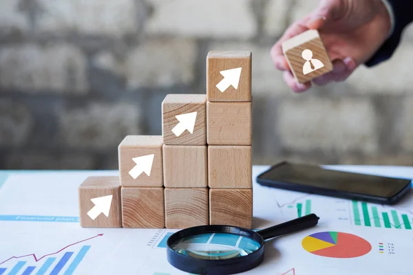 Business concept growth success process, man hand arranging wood block stacking with icon arrow on paper chart closeup.