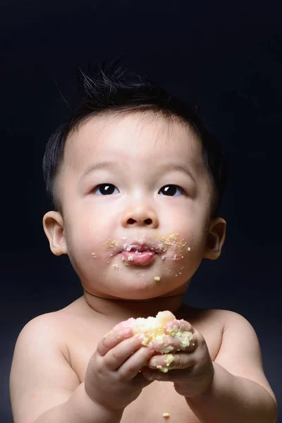 Sød asiatisk baby dreng spiser kage med sin både hånd og rodet på - Stock-foto