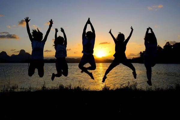 Silhouette d'amis sautant au coucher du soleil Image En Vente
