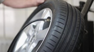 Araç tamircisinin otomobil servisinde alaşımlı tekerlekle lastiği pompalama görüntüsü.