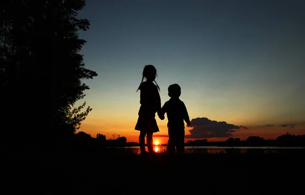 Silhouetten von zwei Kindern, die sich an Händen halten — Stockfoto